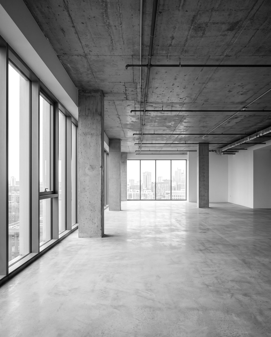 An empty open-plan office floor with concrete columns and floor-to-ceiling windows